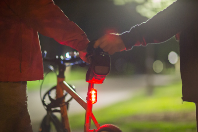 Photograph of two people holding onto the same bike, which has a red bike light, in the dark