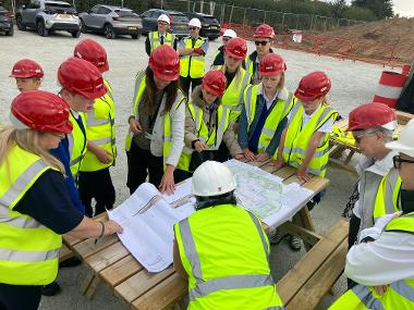 school children in high vis jackets and hard hats look at plans