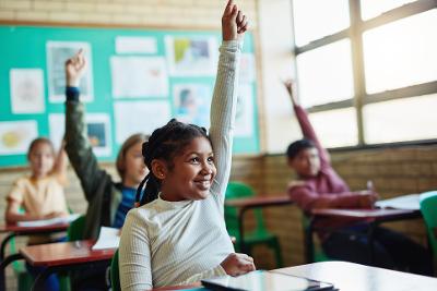 A classroom of smiling children putting up their hands