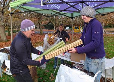 Photo of a person handing a tree pack to another person along with bamboo canes and guards