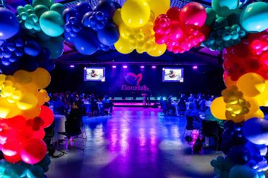 The event stage with two large screens showing the Flourish logo viewed through a balloon arch